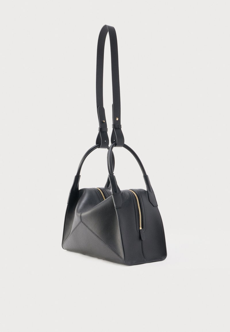Sac à main en cuir noir avec double poignée et une longue bandoulière ajustable, doté d'une fermeture éclair dorée.