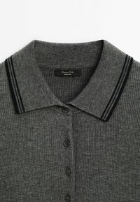 Polo gris en tricot avec un col classique à rayures noires, six boutons noirs et un tissu texturé. Étiquette de la marque visible.
