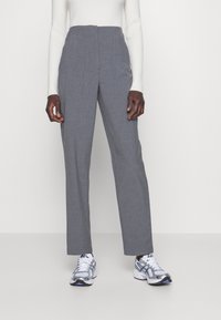 Grijze op maat gemaakte broeken met een hoge taille, riemlussen en plooien; gecombineerd met een witte geribde longsleeve en grijs/blauwe sportschoenen.