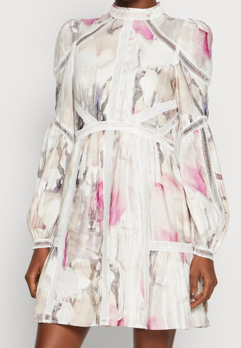 Sukienka w kwiatowy wzór z lekkiego materiału, w odcieniach różu i beżu, z długimi bufkami i koronkowym wykończeniem wzdłuż szwów.