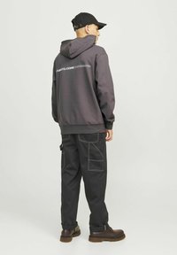 Grijze hoodie met een buidel en grote capuchon, met witte tekst op de achterkant. Gecombineerd met zwarte cargobroek en bruine laarzen.