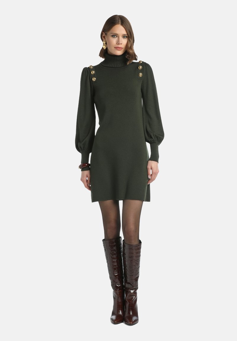 Grünes Strickkleid mit hohem Kragen, puffigen Ärmeln und goldenen Knopf-Details. Getragen mit dunkelbrown Kniehohen Stiefeln im Krokodil-Muster.