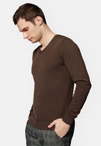 Brązowy sweter z dekoltem w serek, wykonany z dzianiny, dopasowany krój z długimi rękawami i ściągaczami, z minimalistycznym logo na piersi.