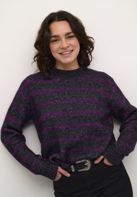 Donkergrijs gestreept sweater met paarse strepen, met een ronde hals en ribgebreide manchetten, gedragen met hoge zwarte broeken en een riem.