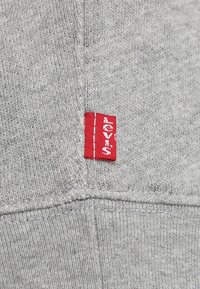 Tissu de sweat-shirt gris avec une texture douce et une �étiquette Levi's brodée rouge visible près de la couture. Présente un design décontracté et des coutures soignées.