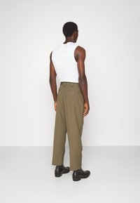 Witte mouwloze shirt gecombineerd met olijfgroene broeken; de broeken hebben een hoge taille, rechte pijpen en achterzakken; zwarte enkellaarsjes.