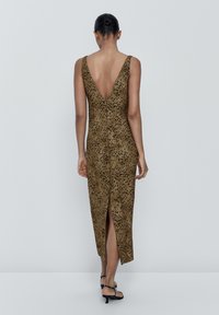 Robe sans manches marron avec un dos en V profond, présentant un motif à pois, une fente à l'avant et une texture douce. La longueur arrive au milieu du mollet.