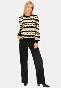 Sweter w czarno-kremowy wzór zygzak, z długimi rękawami, połączony z czarnymi spodniami typu wide-leg i czarnymi botkami do kostki. Gładka tekstura.