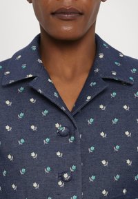 Navyblauwe spijkerjack met kleine geborduurde bloempatronen in groen en wit. Voorzien van een puntig kraag en knoopsluiting.