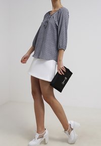 Blouse bleue à motifs avec des manches trois-quarts, associée à une mini jupe blanche et une pochette noire. Chaussures à talons blanches avec des accents en mesh.