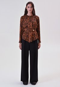 Top con stampa leopardo in arancione e nero, con cintura in vita, abbinato a pantaloni neri a gamba larga. Tessuto liscio con maniche lunghe e scollatura rotonda.