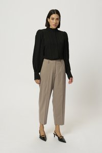Blouse noire à côtes avec des manches ballon, col montant et fermeture à bouton, portée avec un pantalon beige à rayures et des escarpins noirs à bride.