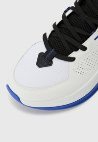 Baskets blanches en cuir et maille, avec des lacets noirs, des accents bleus et des détails perforés sur le dessus.