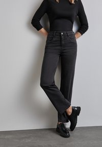 Jeans negros de talle alto con un diseño de pierna recta, que cuentan con bolsillos delanteros, un cierre de botón y un ligero desvanecimiento. Combinados con zapatos negros.
