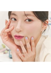 Modèle à la peau claire et aux cheveux foncés, portant un haut beige. Les ongles présentent un dégradé de bleu clair à rose pastel avec un ongle accent scintillant.