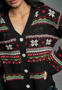 Sort cardigan med et festligt mønster i rød, grøn og hvid, v-hals og fem dekorative knapper. Tekstureret strikdesign.