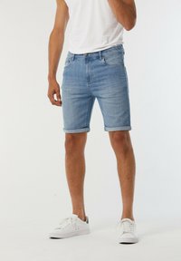 Shorts en denim bleu clair avec ourlets retroussés, design ajusté, style à cinq poches et légers décolorations. Associés à des baskets blanches.