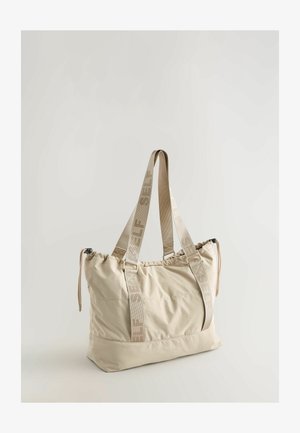 Beige fabric tote bag with a gathered top, dual straps labeled "SELF," and a smooth texture. Features a square-shaped body for ample storage.