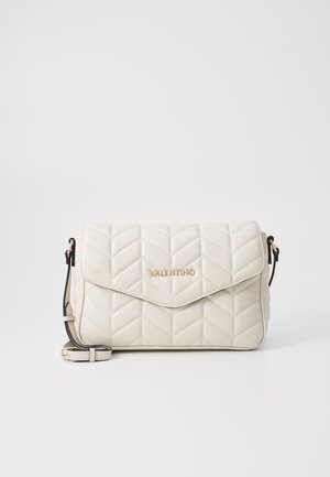 Sac à main en cuir crème matelassé avec une fermeture à rabat, arborant un logo doré, une bandoulière noire et un motif en chevrons. Design compact et rectangulaire.