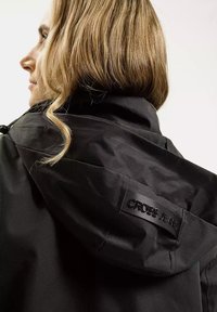 Czarna kurtka z kapturem o gładkiej fakturze, z metką logo "CROSS JEANS" z tyłu, charakteryzująca się minimalistycznym designem i eleganckim wyglądem.