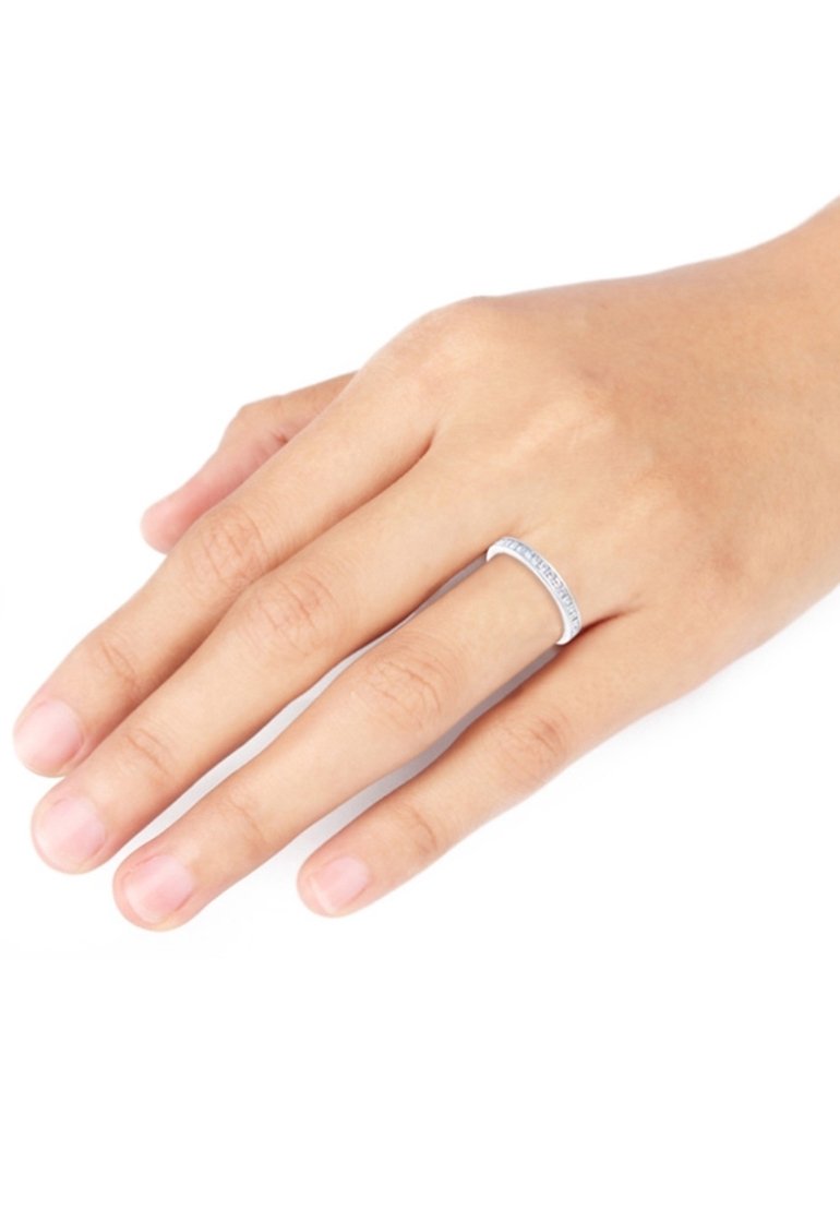 Main à la peau claire portant une fine bague en argent avec de petites pierres incrustées sur l'annulaire sur fond blanc.