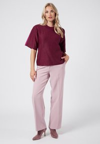 Top magenta de manga corta con un acabado texturizado, combinado con pantalones ajustados rosa claro y tacones de punta a juego.