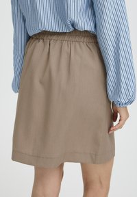 Mujer que lleva una falda beige hasta la rodilla con cintura elástica y una camisa de manga larga azul con rayas verticales negras.