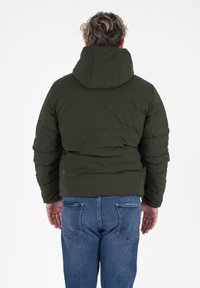 Olijfgroen pufferjack met een capuchon, met een gequilt textuur en een cropped ontwerp. Gecombineerd met blauwe denim jeans.