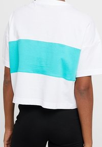 Zkrácený bílý tričko s tyrkysovým vodorovným pruhem, kulatým výstřihem a krátkými rukávy. Měkká látka s ležérním designem.