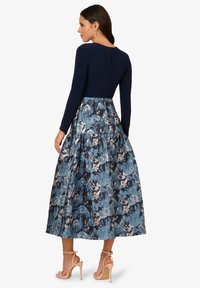 Ein marineblaues langes Kleid mit einem strukturierten Rock in blauen Blumenmustern, das einen taillierten Oberteil und einen Reißverschluss an der Rückseite aufweist.