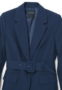 Giacca blu navy con vita cintura, due tasche frontali e design classico con rever. Realizzata in un tessuto liscio con una vestibilità strutturata.