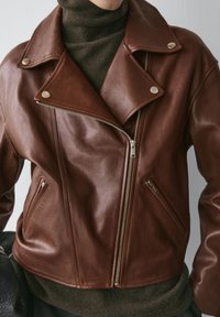 Giacca da motociclista in pelle marrone con finitura opaca, cerniera asimmetrica e dettagli in argento. Presenta due tasche laterali con cerniera e ampie pettorine.