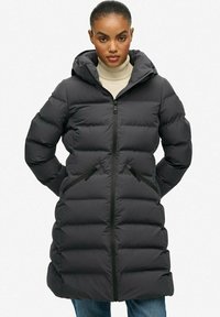 Sort puffjakke med hætte, med lynlås foran, sidelommer og et quiltet mønster. Fremstillet af et glat, isoleret materiale.