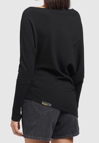 Pull noir à manches longues en maille avec un large col et des poignets côtelés, associé à un short en denim foncé avec un design de poche cousue.