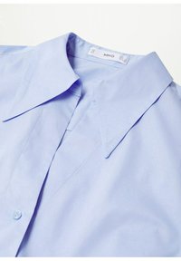 Chemise bleu clair à col avec fermeture boutonnée à l'avant, col visible et étiquette de marque MNG à l'intérieur de l'encolure.