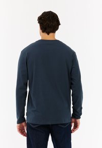 Langsleeve marineblauw T-shirt van katoen, met een ronde hals en rechte snit, gezien van de achterkant met zichtbare stikdetails.