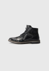 Botín negro de cuero con cordones, de tacón bajo y panel lateral con logo, sobre un fondo liso gris claro.