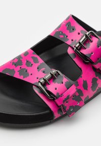 Svart och rosa sandal med prickigt mönster, som har två justerbara remmar, metallspännen och en texturerad sula.