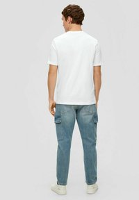 White short-sleeve T-shirt paired with light blue cargo pants featuring side pockets, worn with white sneakers. Neutral gray background.