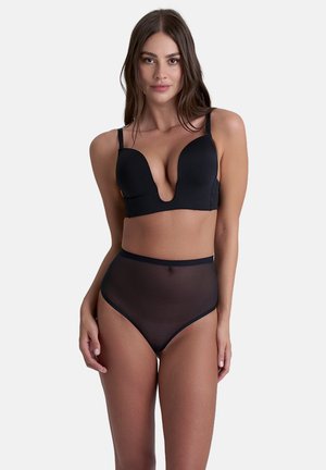Completo di lingerie nera con reggiseno a scollo profondo e bretelle regolabili, e perizoma alto in tessuto trasparente, che mette in risalto le texture morbide.