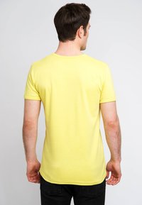 Yellow short-sleeve t-shirt with a round neckline, made from cotton, featuring a smooth texture and a fitted shape, paired with dark jeans.