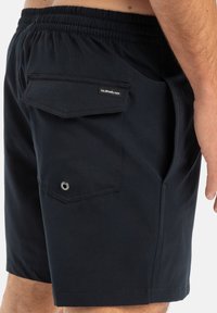 Sorte svømmedraktshorts med elastisk linning, sidelommer og en baklomme med klaff og logoetikett. Laget av lett materiale.