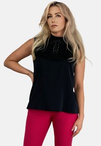 Czarny bezrękawnik z falbaniastym dekoltem zdobionym koralikami; w zestawie z dopasowanymi różowymi spodniami. Gładka faktura i luźny krój.