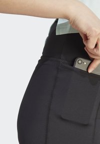 Sorte treningsleggings med en side-lomme som passer til en smarttelefon. Stoffet er glatt med synlige sømdetaljer.