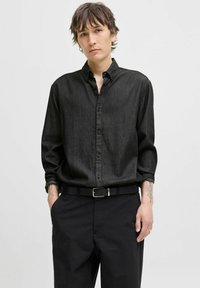 Cămașă neagră cu nasturi, dintr-un material ușor, periat, cu textură vizibilă, asortată cu pantaloni negri largi și un curea neagră.