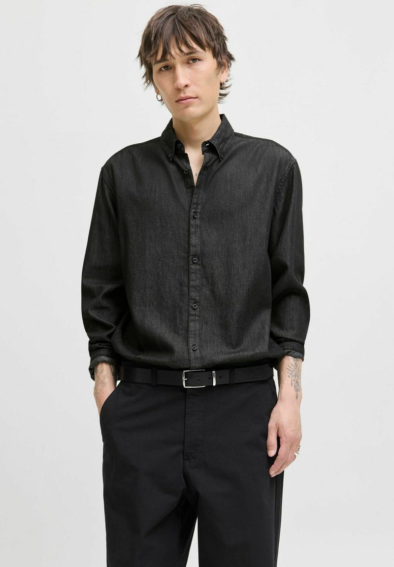 Camicia nera a maniche lunghe in un tessuto leggero e spazzolato con texture visibile, abbinata a pantaloni neri larghi e una cintura nera.