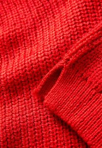 Tessuto a maglia rosso con una texture a coste, caratterizzato da dettagli cuciti e diverse trame di punto per una maggiore dimensione e profondità.