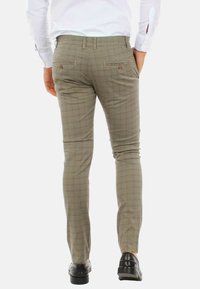 Pantaloni slim-fit in marrone chiaro con un sottile motivo a quadri. Presentano tasche posteriori con chiusura a bottone e una texture di tessuto liscia.
