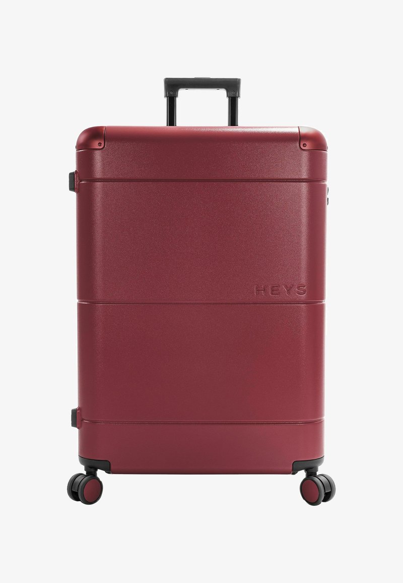 Valise rigide bordeaux avec quatre roues pivotantes noires et bordeaux et poignée télescopique, logo "HEYS" embossé à l'avant.