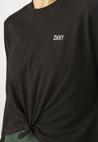 Svart långärmad t-shirt i mjuk bomull, med en knuten detalj vid midjan och en liten vit broderad "DKNY"-logotyp.